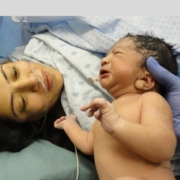 A woman tenderly holds a baby next to an incubator, capturing an intimate moment of care in a hospital setting.