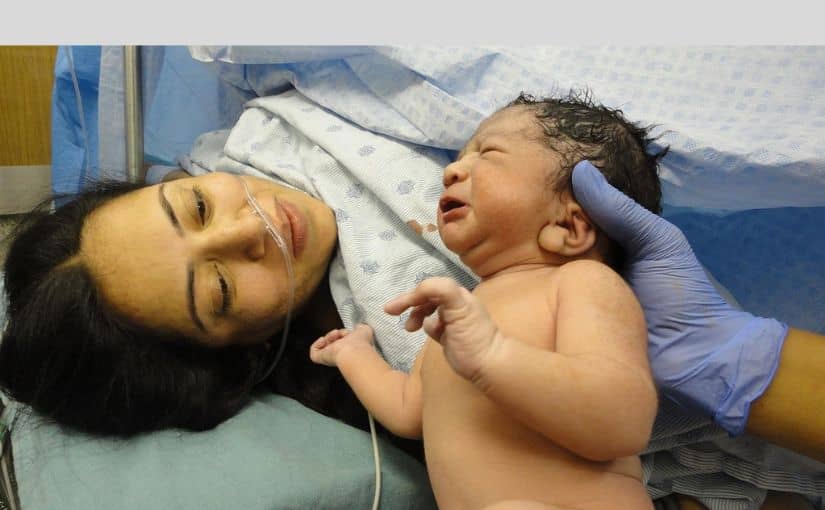 A woman tenderly holds a baby next to an incubator, capturing an intimate moment of care in a hospital setting.