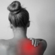 A woman grimaces, holding her shoulder, indicating discomfort and pain.
