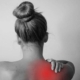 A woman grimaces, holding her lower back, indicating discomfort and pain.