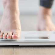 A person stands on a scale, balancing with her toes at the top, indicating she is checking her weight.