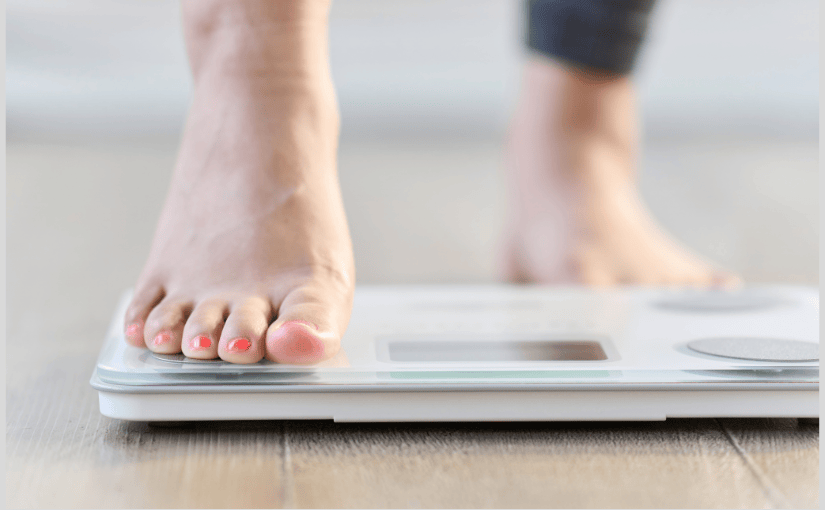 A person stands on a scale, balancing with her toes at the top, indicating she is checking her weight.
