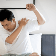 Man sitting on a bed, visibly distressed, holding his lower back due to pain.
