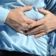 A person in a blue shirt and tie is holding his stomach, appearing to be in discomfort or pain.