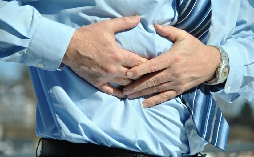 A person in a blue shirt and tie is holding his stomach, appearing to be in discomfort or pain.
