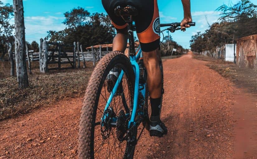 A man cycling down a dirt road surrounded by greenery and trees.