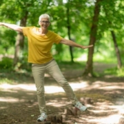 A man in a yellow shirt joyfully jumping in a lush green forest surrounded by trees