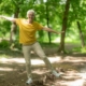 A man in a yellow shirt joyfully jumping in a lush green forest surrounded by trees