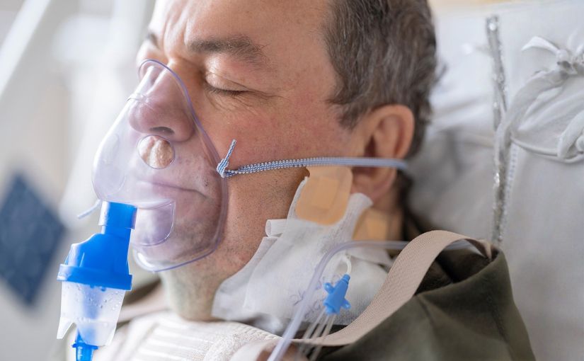 man lying in a hospital bed, wearing an oxygen mask, appears to be receiving medical care.
