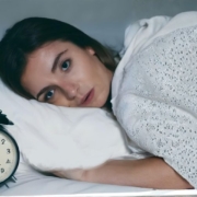 A person lying in bed next to an alarm clock, appearing relaxed and ready to start her day.