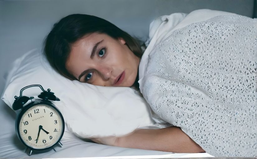 A person lying in bed next to an alarm clock, appearing relaxed and ready to start her day.