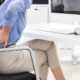 person holding lower due to pain and discomfort while sitting on office chair