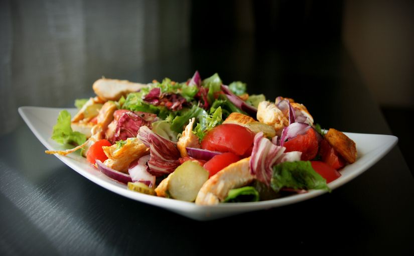 A fresh salad featuring grilled chicken, ripe tomatoes, and crisp lettuce arranged in a bowl