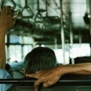 passenger sitting on a bus with one arm resting over the seat back and another hand holding a overhead handle.