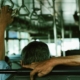 passenger sitting on a bus with one arm resting over the seat back and another hand holding a overhead handle.