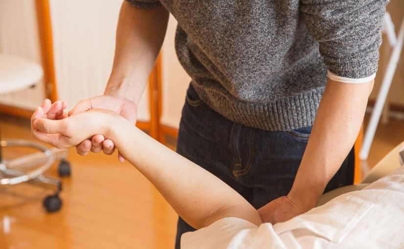 close-up shot of a practitioner wearing a grey sweater holding and examining a patient's arm and wrist during a chiropractic session.